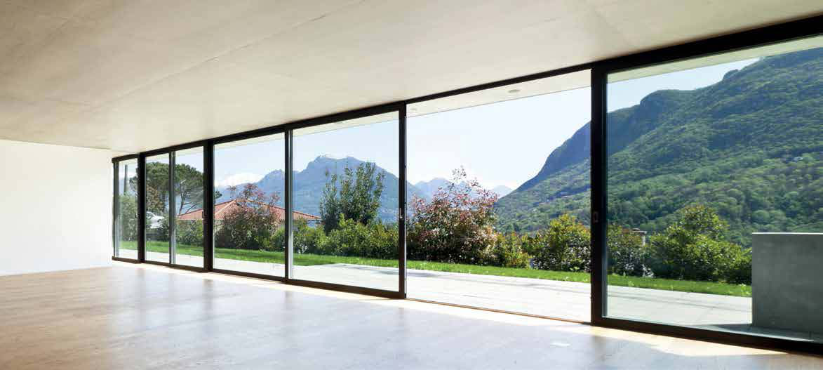 Wide sliding glazing opening a bright interior to a mountain landscape, from the Synergic collection brochure